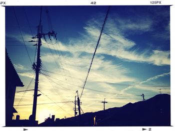 Low angle view of electricity pylon against cloudy sky