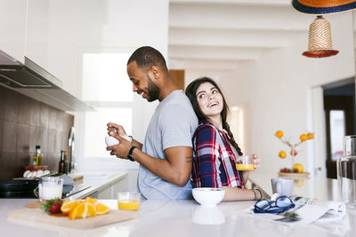 Young couple having breakfast in the kitchen, standing back to back
