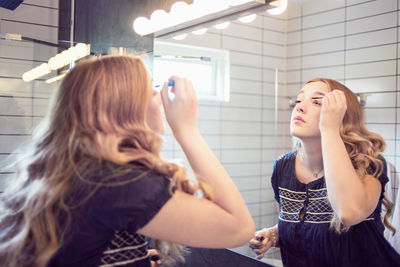 Young woman applying mascara in front of bathroom mirror