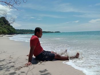 Full length of man on relaxing on beach against sky