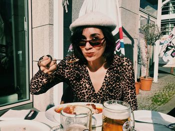 Portrait of young woman eating food while sitting at outdoor restaurant