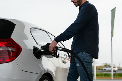 Cropped unrecognizable man refilling vehicle tank at petrol station during energy crisis