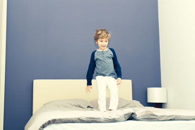 Full length of boy standing on bed at home