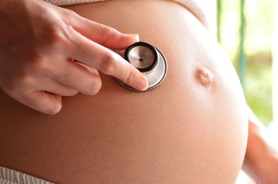 Close-up of pregnant woman hand holding stethoscope over abdomen