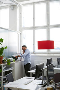 Businessman talking on phone while reading document at creative office