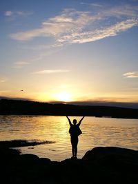 Rear view of silhouette man standing by lake against sky during sunset