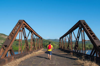 Rear view of man walking on bridge against clear sky