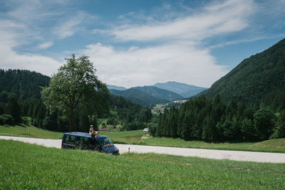 Woman looking at view while sitting on car roof against sky