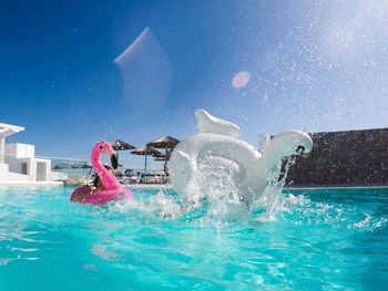 Inflatable rings splashing water in swimming pool against blue sky
