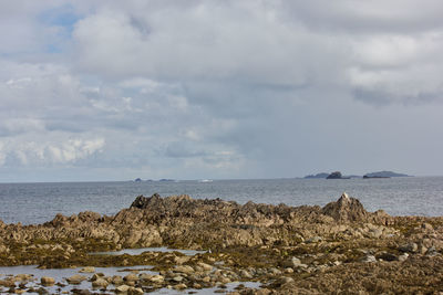 Scenic view of sea and rocks against cloudy sky