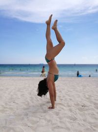 Full length of young woman doing handstand at beach against sky