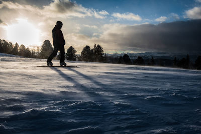 Silhouette man snowboarding on snow against sky during sunset