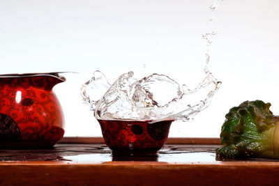 Close-up of water splashing on table against white background