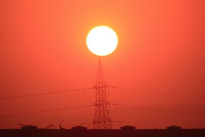 Low angle view of silhouette of electricity pylon against orange sky