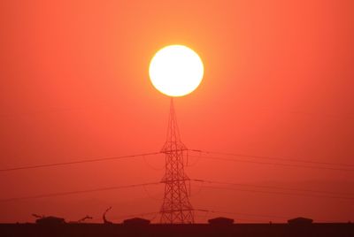 Low angle view of silhouette electricity pylon against orange sky