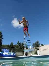 Low angle view of shirtless man jumping in swimming pool against sky