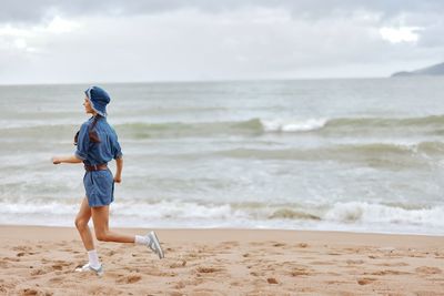 Rear view of woman standing at beach against sky