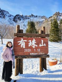 Woman standing by signboard on snow covered land against mountain