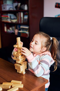 Cute girl playing block while sitting on table at home