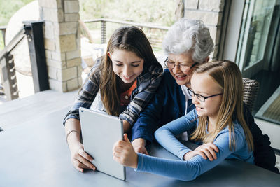 High angle view of granddaughters using tablet computer with grandmother on porch