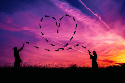 Silhouette people standing on field against sky during sunset