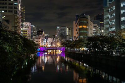 Illuminated bridge over river in city at night