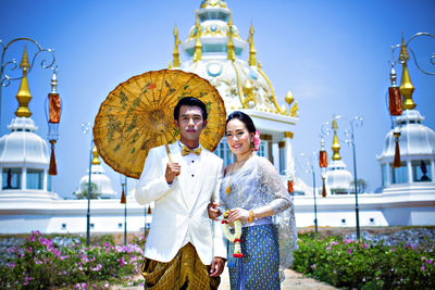 Portrait of couple with umbrella standing against temple