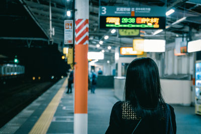 Rear view of woman standing at railroad station