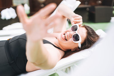 Stylish woman plus size body positive in black swimsuit and sunglasses on beach lounger near pool