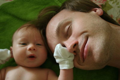 Close-up of father with baby boy sleeping on bed