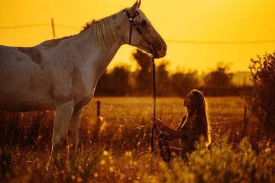 Side view of woman in field against sky during sunset