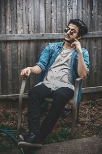 Young man wearing sunglasses sitting on chair at yard