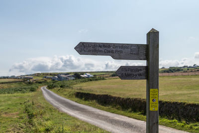 Road sign on field against sky