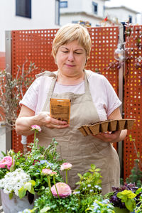 Senior plus size retired woman planting flower seeds in peat tray. terrace gardening,  hobby 