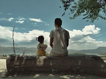 Rear view of couple sitting on land against sky