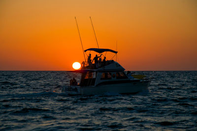 Silhouette people on boat in sea against orange sky during sunset