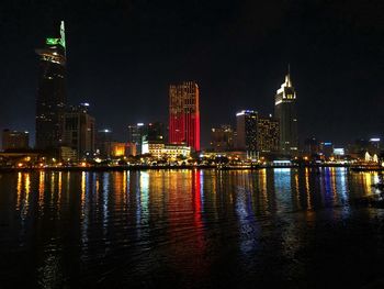 Illuminated buildings by river against sky at night