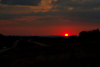 Scenic view of silhouette field against orange sky
