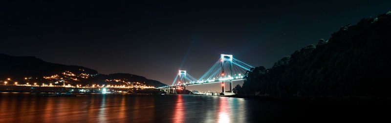 Illuminated bridge over river against sky at night