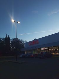 Illuminated street lights by road against sky at dusk