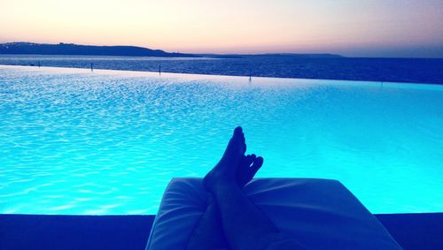 Low section of man relaxing by sea against sky