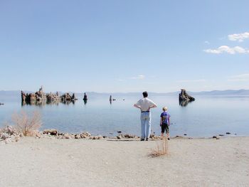 Rear view of father with son standing at beach against sky