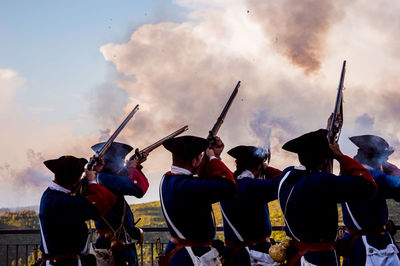 Men wearing traditional clothing while shooting riffles against sky