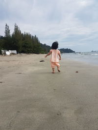 Rear view of boy standing on beach against sky