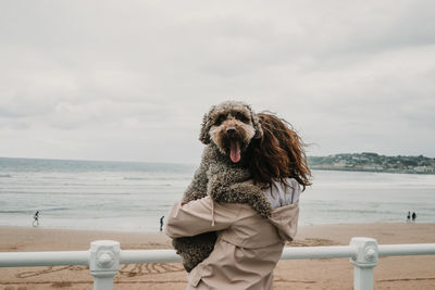 Woman carrying dog while standing at beach