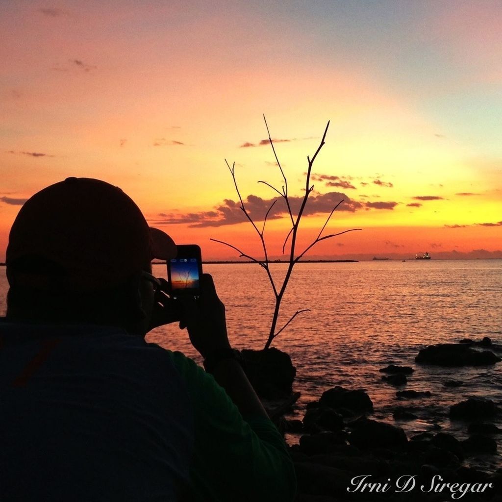 sunset, silhouette, water, orange color, sky, lifestyles, leisure activity, men, sea, scenics, beauty in nature, tranquility, tranquil scene, nature, sitting, idyllic, holding, photographing