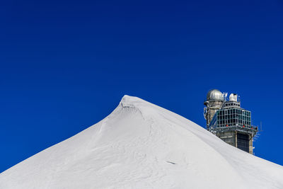 Low angle view of sphinx observatory on snowcapped mountain against clear blue sky
