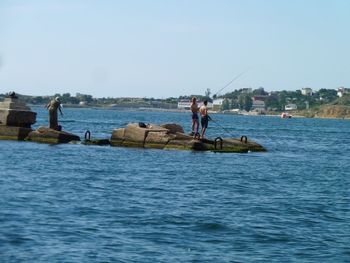 People fishing in sea against clear sky