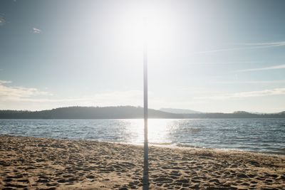 Sun hidden behind blue pole on sandy beach at sea. forest hill on island in background. vivid colors