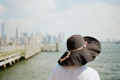 Rear view of mature woman wearing hat looking at sea while standing against sky